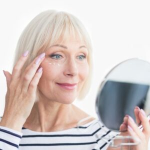 Stem Cell Therapy for Aging woman applying anti-wrinkle cream under her eye while looking in a hand mirror