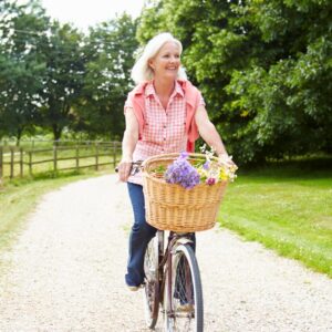 Wellness & Longevity middle-aged woman riding a bike on a gravel path with flowers in the basket