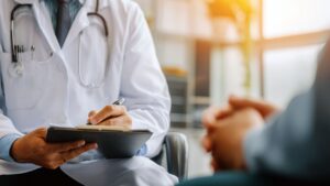 close-up of doctor’s hands writing on a clipboard during a patient consultation