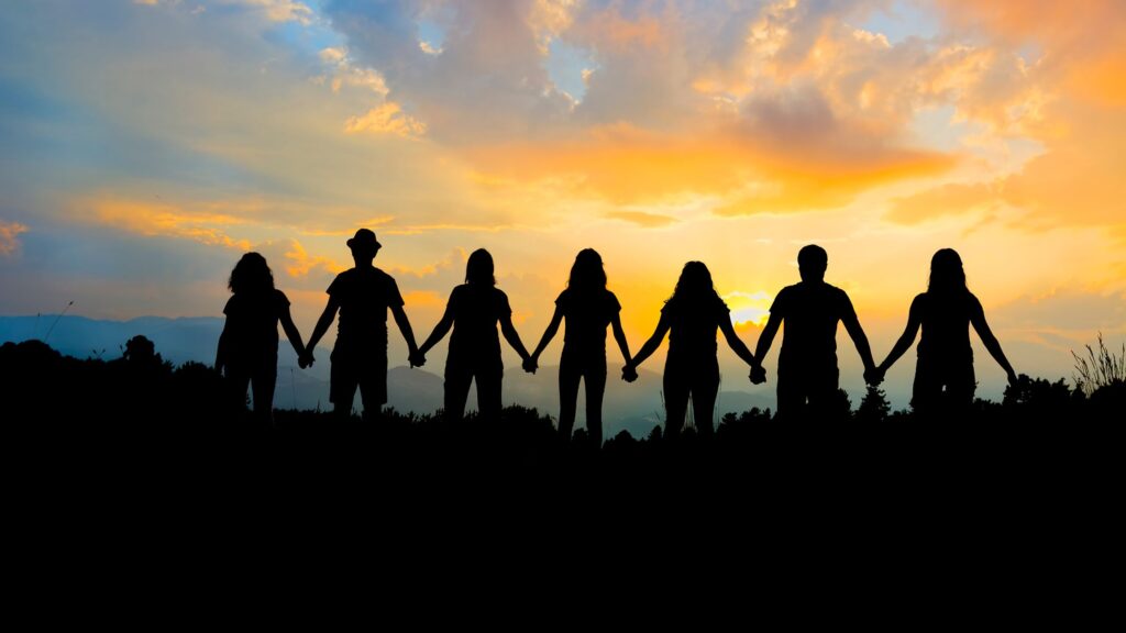 silhouette of a group of people holding hands in a field at sunset
