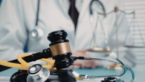 gavel and a stethoscope resting on a clipboard with a blurred background of a medical professional in an office